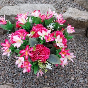 May include: A bouquet of pink and white artificial flowers arranged in a cluster. The flowers are surrounded by small grey stones.