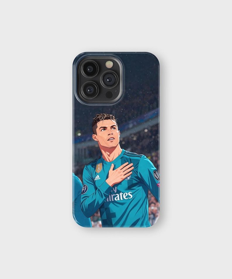 May include: A phone case featuring an illustration of a soccer player in a teal jersey with the Emirates logo. The player is depicted with his hand over his heart, set against a stadium background.