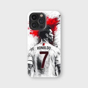 May include: A white phone case featuring a stylized image of a soccer player with the name "RONALDO" and the number "7" on the back of his jersey. The design includes red paint splatter accents.