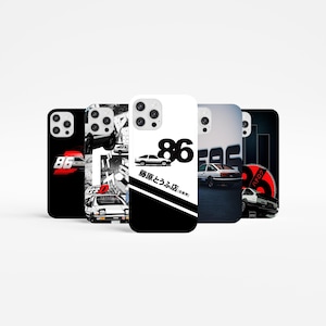 Może przedstawiać: Pięć różnych etui na telefon z czarno-białym wzorem i czerwonym akcentem. Etui przedstawiają samochód, liczbę 86 i japoński tekst. Etui są przeznaczone do modeli iPhone'a z wystającym aparatem.