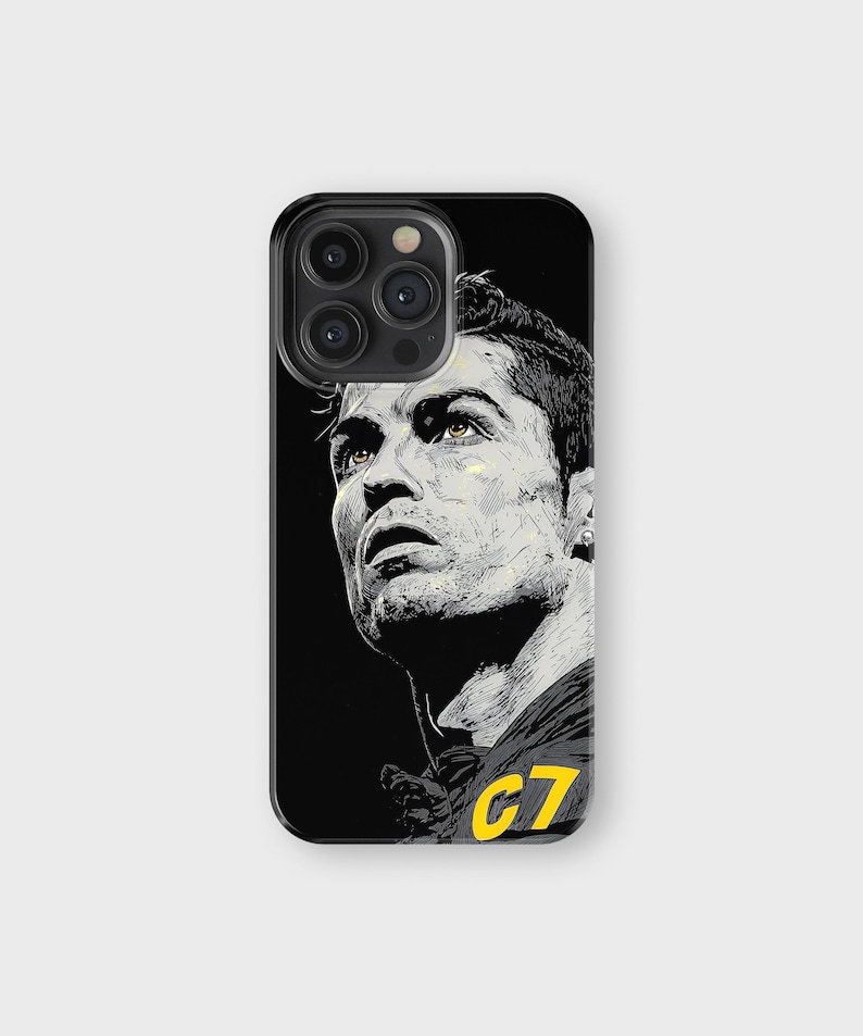 May include: Black phone case featuring a stylized portrait of a soccer player. The portrait is in black and white with yellow accents, including the number "C7" on the jersey. The phone case has a glossy finish.