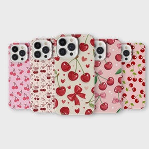 Könnte beinhalten: Eine Auswahl an Handyhüllen mit Kirschmustern. Die Hüllen zeigen Designs von Kirschen, Schleifen und Herzen in Rosa-, Rot- und Cremetönen. Diese Hüllen sind für ein Smartphone konzipiert.