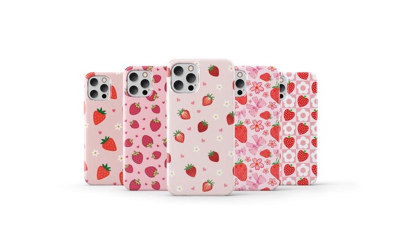 May include: Five different phone cases with a pink background and a pattern of red strawberries. The cases are all for the same model phone and have different patterns of strawberries.