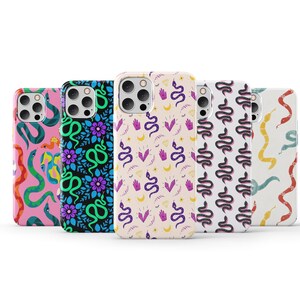 May include: Five different phone cases with snake patterns. The cases are all for the iPhone 13 Pro Max and feature different colours and designs. The cases are all made of a clear, flexible material and have a raised lip around the camera lens to protect it from scratches.