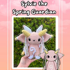 May include: A light pink crochet plush toy named Sylvie the Spring Guardian with large dark eyes, yellow and white horns, and long braided yarn hair. The creature features a white spiral on its chest and white accents on its feet and ears.