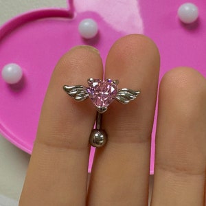 May include: A silver belly button ring with a pink heart-shaped gem and small wings on either side.