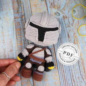May include: Crochet pattern for a gray and brown amigurumi figure wearing a helmet with a black visor. The pattern is available in English and French. The pattern is a PDF download.