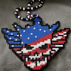 May include: A handmade pendant featuring a patriotic design, crafted from colorful beads. The pendant showcases a blue field with white stars, red and white stripes, and a black outline. A beaded lanyard in matching colors is attached.