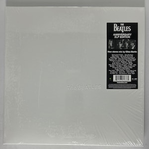 May include: White vinyl record album cover with the text "The Beatles" in black lettering. The back of the album cover features a photo of the Beatles and a list of songs included on the album. The album is titled "The Beatles Anniversary 2LP Edition" and features a new stereo mix by Giles Martin.