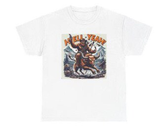 May include: White t-shirt featuring a colorful graphic of a creature riding a bull with the text "HELL YEAH!". The illustration has an orange, brown, and blue color palette, with a mountain backdrop. The shirt is made of a soft, comfortable material.