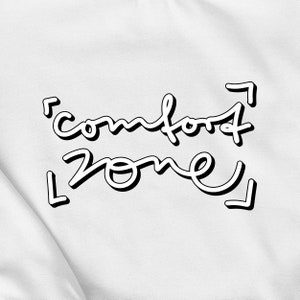 Könnte beinhalten: Weißes T-Shirt mit schwarzem Text, der "comfort zone" mit Pfeilen auf beiden Seiten der Wörter sagt.