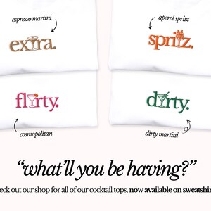May include: Four white t-shirts with different cocktail-themed designs. The designs include "extra", "flirty", "spritz", and "dirty". The text "what'll you be having?" is written below the shirts. The text "check out our shop for all of our cocktail tops, now available on sweatshirts!" is written below the text.