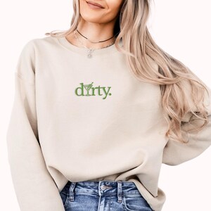 May include: A beige sweatshirt with a green embroidered design that says "dirty."
