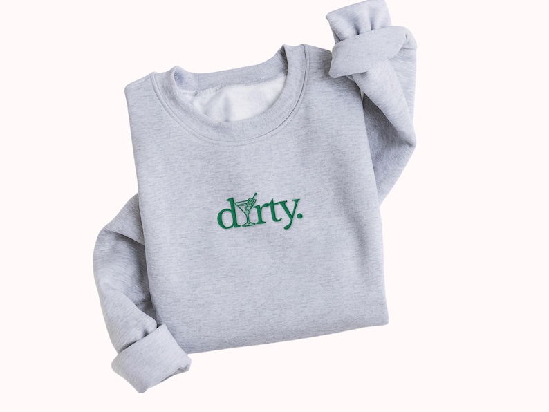 May include: A grey sweatshirt with a green embroidered design that says "dirty." The design includes a martini glass with a green olive.