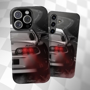 Peut inclure: Deux coques de téléphone représentant une voiture de sport argentée avec des feux arrière rouges, sur un fond de route noir et blanc flou. Le mot "Supra" est visible. Les coques ont une finition brillante.