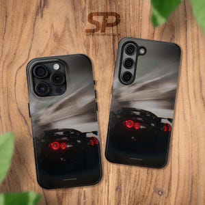 Op de afbeelding: Twee zwarte telefoonhoesjes met een wazig beeld van een zwarte sportwagen met rode achterlichten. De auto rijdt op een weg met een bewegingsonscherpte-effect. De hoesjes hebben een camera-uitsparing aan de achterkant.