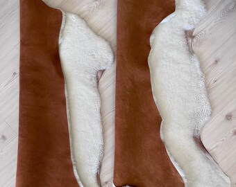 May include: Two sheepskin rugs with a brown suede backing. The rugs are laid out on a light wood floor.