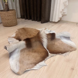 May include: A brown and white animal hide rug with a natural, soft texture. The rug is folded in half and laid out on a light wood floor.