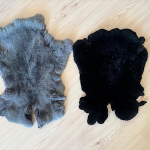 May include: Two rabbit fur pelts, one gray and one black, laid out on a wooden floor.