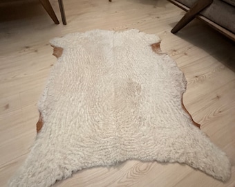 May include: A white faux fur rug with a brown leather border. The rug is laid out on a light wood floor.