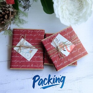 May include: Three gift boxes wrapped in red paper with handwritten text and tied with twine. Each box has a small card attached with a bicycle or flamingo illustration. The word "Packing" is written in blue script at the bottom.