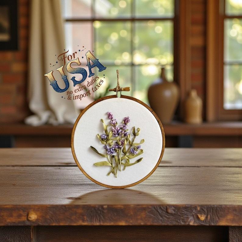 May include: A round embroidery hoop featuring a lavender floral design. The artwork is made with purple and green ribbons on a white fabric background. The hoop is made of wood and has a hanging loop.