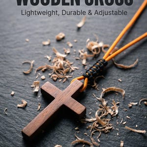 May include: A minimalist wooden cross pendant with an orange cord, lying on a dark surface scattered with wood shavings. The cross is made of dark wood and is lightweight, durable, and adjustable. The text "MINIMALIST WOODEN CROSS" is visible.