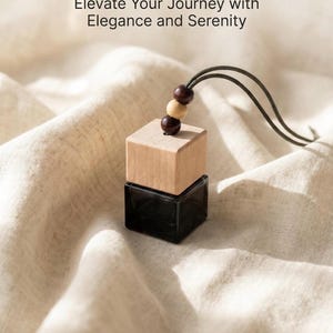 Pode incluir: Um frasco quadrado de vidro preto com tampa de madeira clara e um cordão com duas contas castanho-escuras e uma conta bege clara. O texto "Elevate Your Journey with Elegance and Serenity" está impresso acima do frasco de perfume suspenso.
