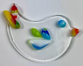 May include: A white glass bird with colorful glass accents. The bird has a yellow, red, and green wing, a blue and white tail, and a blue eye.