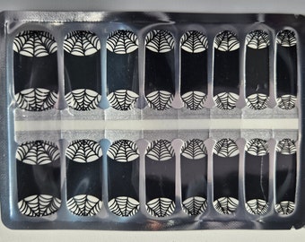 May include: A sheet of black and white nail wraps with a spiderweb design. The wraps are packaged in a silver and white plastic sheet.