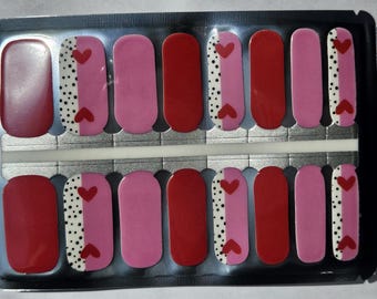 May include: A sheet of nail wraps with a red and pink color scheme. Each wrap features a white and black polka dot design with a red heart on one side and a pink heart on the other.