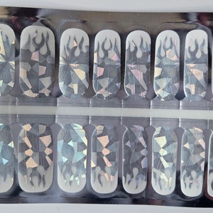 May include: A pack of nail wraps with a holographic, geometric design. The wraps feature a flame design and are packaged in a clear plastic pouch.