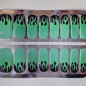 May include: A sheet of 12 green and black nail wraps with a flame design. The nail wraps are in a clear plastic package.