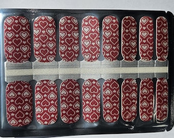 May include: A sheet of red and white nail polish wraps with a heart pattern. The wraps are designed to be applied to fingernails.
