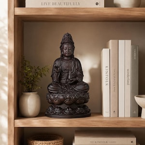 May include: A dark brown Buddha statue seated on a lotus flower base. The statue is on a wooden shelf with books and a small potted plant. The books are titled "Kinfolk" and "Wonderland". The shelf is part of a larger wooden structure.