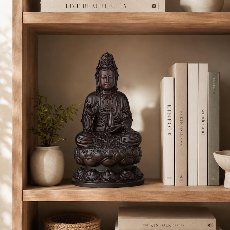 May include: A dark brown Buddha statue seated on a lotus flower base. The statue is on a wooden shelf with books and a small potted plant. The books are titled "Kinfolk" and "Wonderland". The shelf is part of a larger wooden structure.
