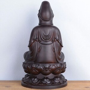 May include: A dark brown statue of a seated figure, viewed from the back. The figure is draped in flowing robes and sits atop a lotus flower base. The statue has a smooth, polished finish and is set against a light background.