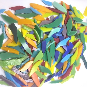 May include: A collection of colorful glass mosaic tiles in various shapes and sizes. The tiles are in shades of green, blue, yellow, orange, and red. The mosaic pieces are scattered on a white surface.