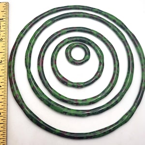 May include: A collection of green and maroon rubber O-rings of varying sizes, arranged concentrically. The rings have a speckled pattern and are displayed against a white background. A ruler is visible on the left side, indicating measurements in inches.