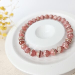 May include: A pink and white striped gemstone bracelet. The bracelet is made of round beads and is on a white surface.