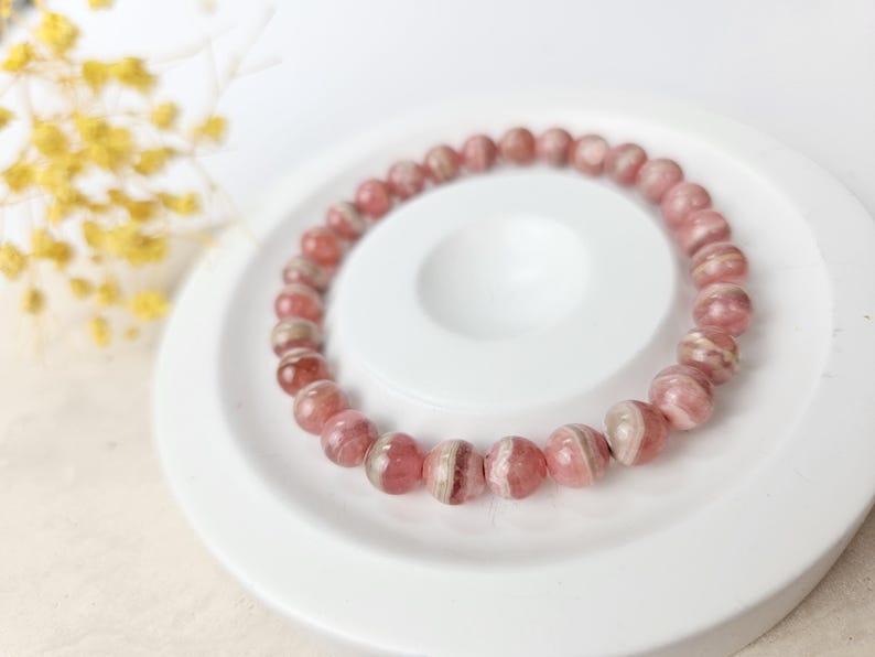May include: A pink and white striped gemstone bracelet. The bracelet is made of round beads and is on a white surface.