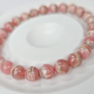 May include: A pink and white gemstone bracelet with round beads. The bracelet is made of natural stones and has a delicate, feminine look.