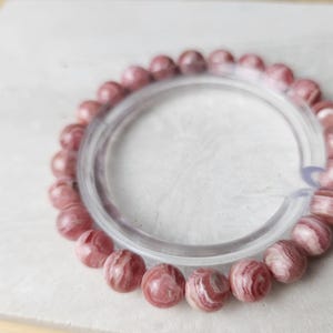 May include: A pink and white striped gemstone bracelet with a clear elastic band.