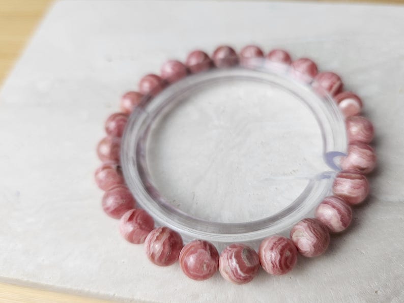 May include: A pink and white striped gemstone bracelet with a clear elastic band.