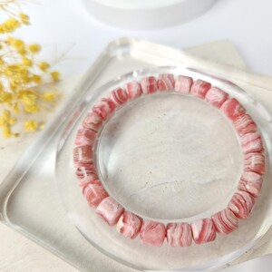 May include: A pink and white striped gemstone bracelet made of round beads. The bracelet is on a clear display stand.