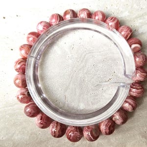 May include: A pink and white striped gemstone bracelet. The bracelet is made of round beads and is strung on a clear elastic cord.