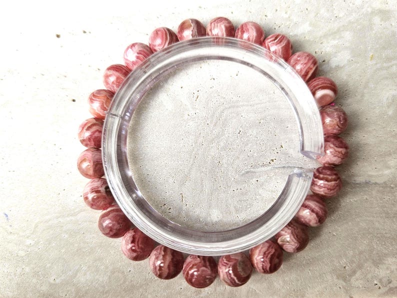 May include: A pink and white striped gemstone bracelet. The bracelet is made of round beads and is strung on a clear elastic cord.