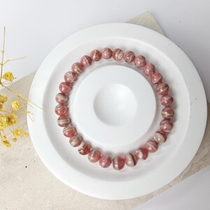 May include: A pink and white striped gemstone bracelet on a white plate. The bracelet is made of round beads.