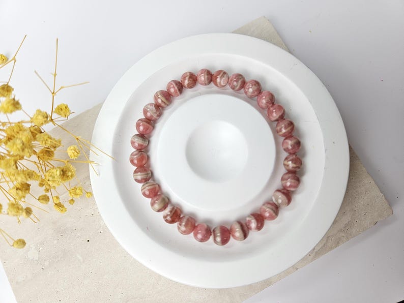 May include: A pink and white striped gemstone bracelet on a white plate. The bracelet is made of round beads.