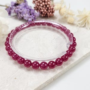 May include: A bracelet made of deep red beads. The beads are round and smooth, and they are strung together on a clear elastic cord.